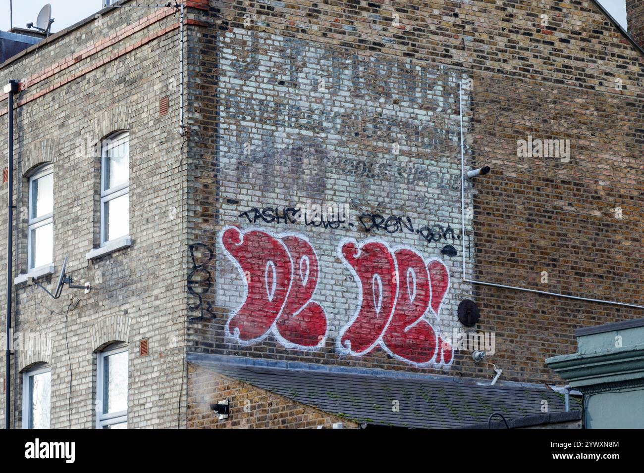Un cartello fantasma che pubblicizza "J. T. Turner, Baker & Confectioner, Hovis, Schools Provided" su un muro in mattoni con estremità a timpano, coperto da graffiti, Londra, Regno Unito Foto Stock