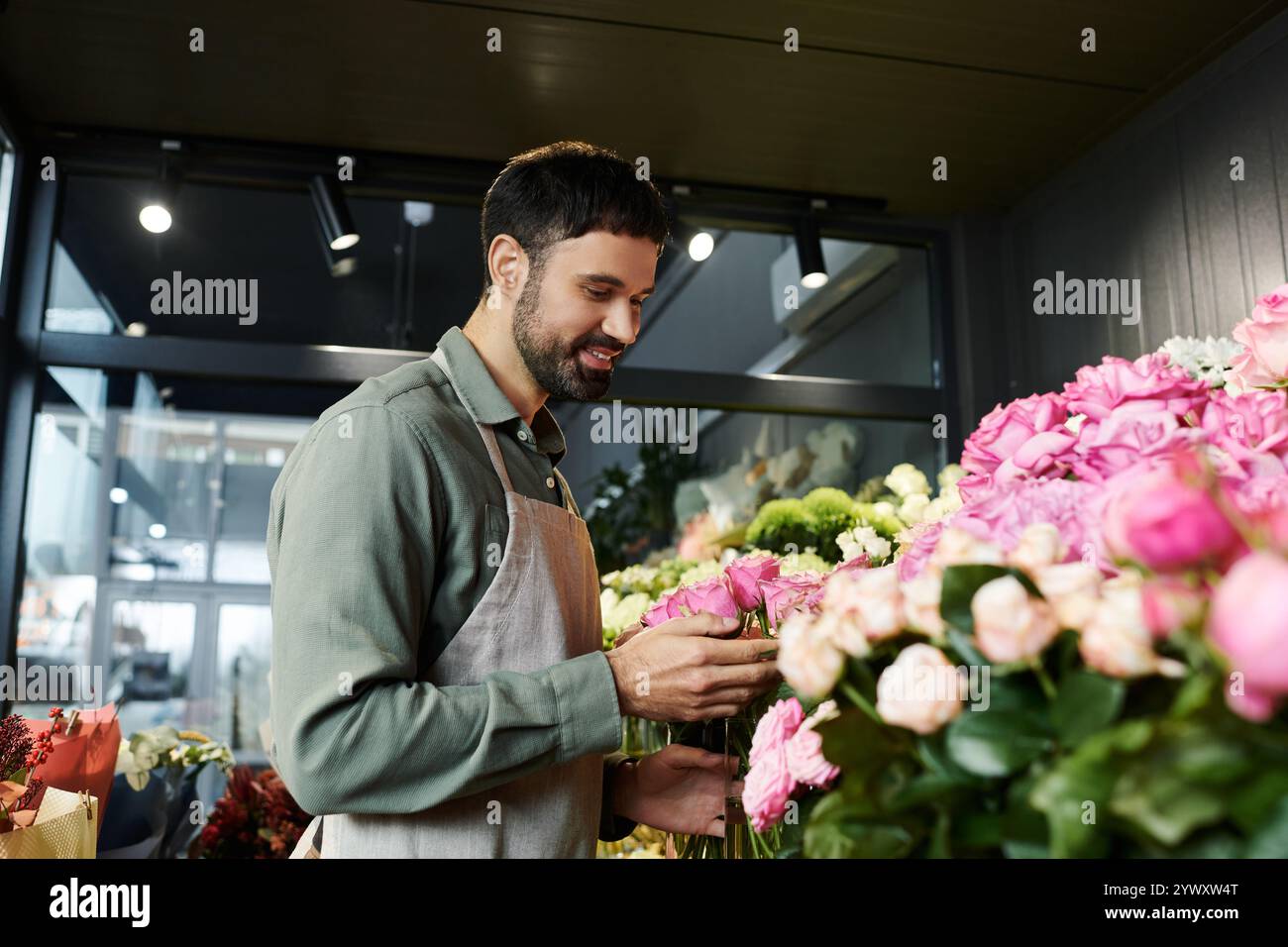 Un uomo barbuto organizza con cura fiori freschi nel suo vivace negozio di fiori, mostrando il suo mestiere. Foto Stock