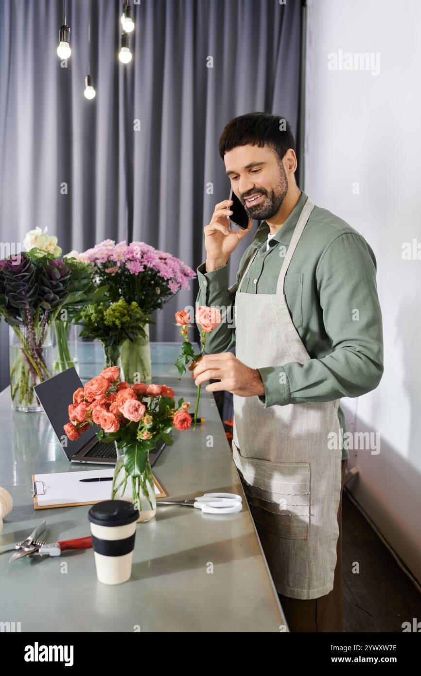 Un uomo barbuto interagisce con i clienti al telefono mentre crea un bellissimo bouquet. Foto Stock