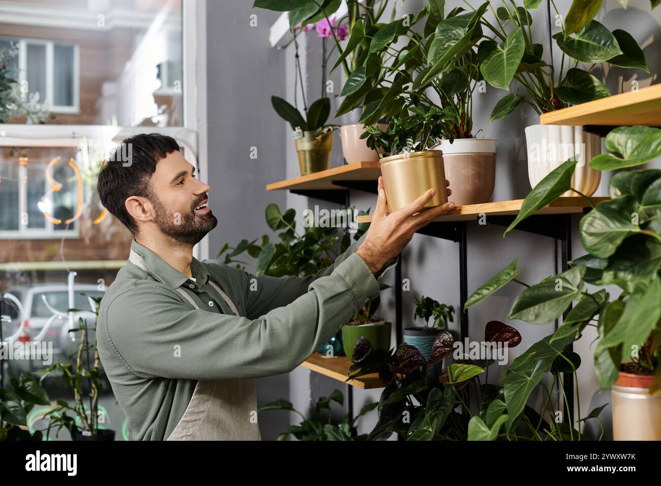 Un uomo barbuto tende a rigogliose piante verdi nel suo affascinante negozio di fiori, mostrando la sua esperienza. Foto Stock