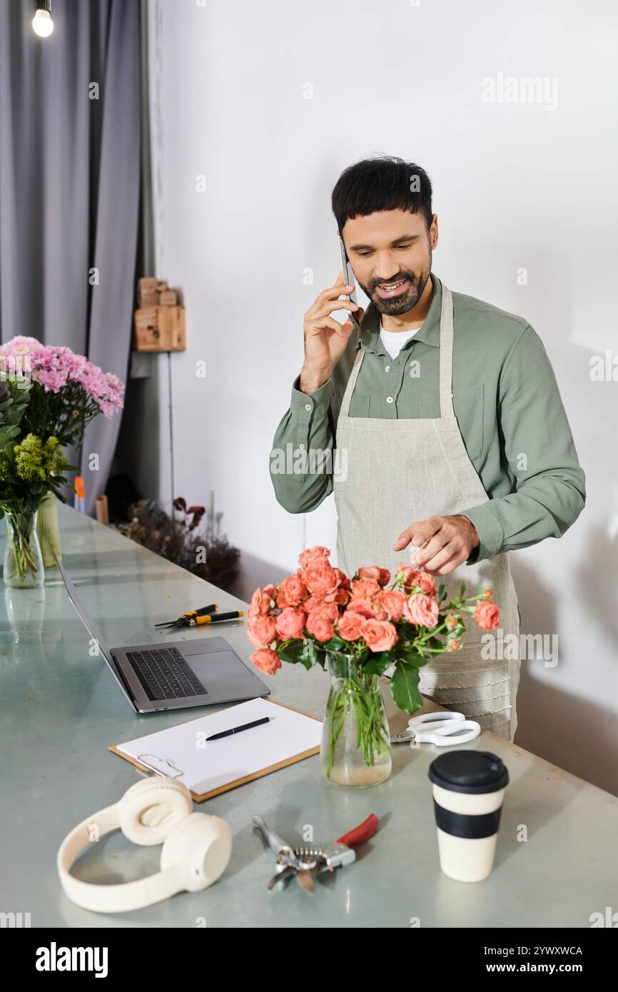 Un bell'uomo barbuto lavora gioiosamente nel suo negozio di fiori, creando un bouquet di rose. Foto Stock