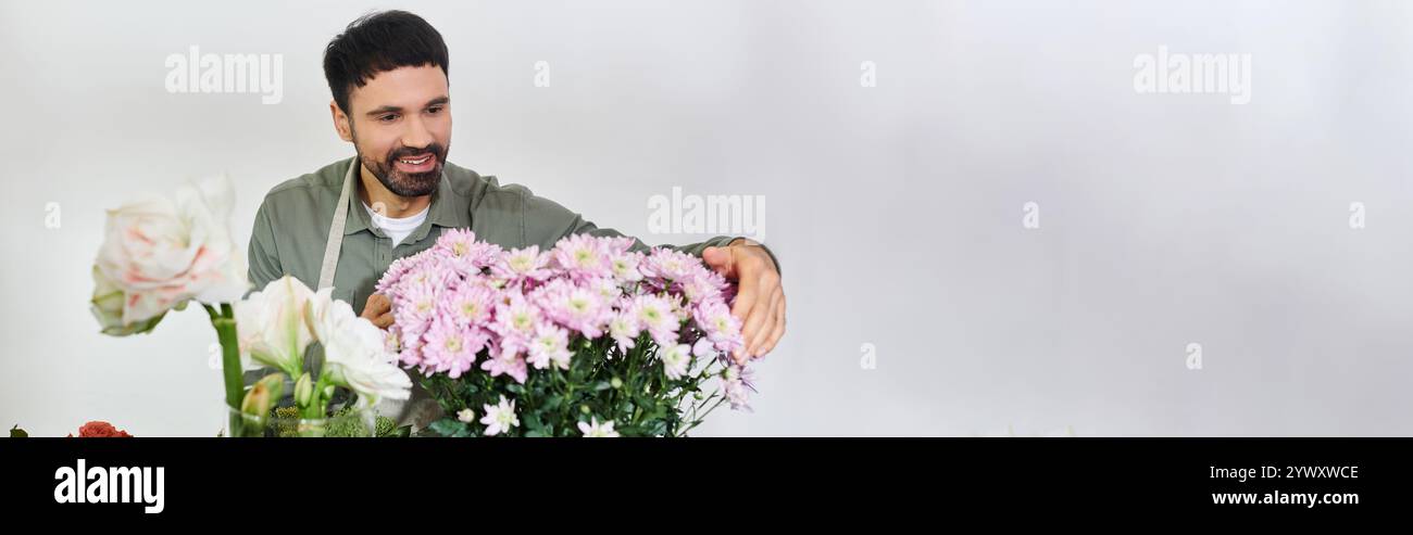 Un bellissimo uomo barbuto realizza con cura composizioni floreali nel suo vivace negozio di fiori, lo striscione Foto Stock