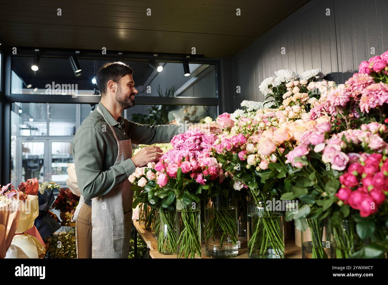 Un bell'uomo barbuto organizza fiori freschi nel suo accogliente negozio, mostrando fiori vivaci. Foto Stock