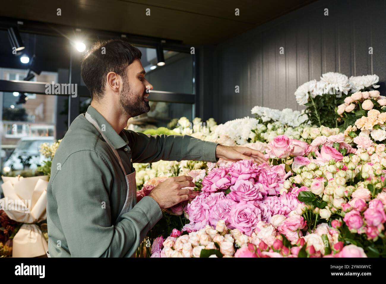 Un fiorista esperto prepara delicatamente splendide rose rosa tra una varietà di fiori nel suo negozio. Foto Stock