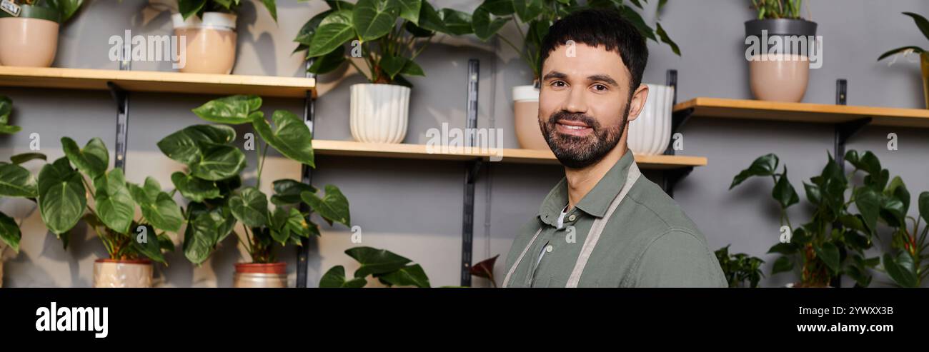 Un fiorista esperto sorride mentre organizza bellissime piante in un vivace negozio pieno di verde Foto Stock