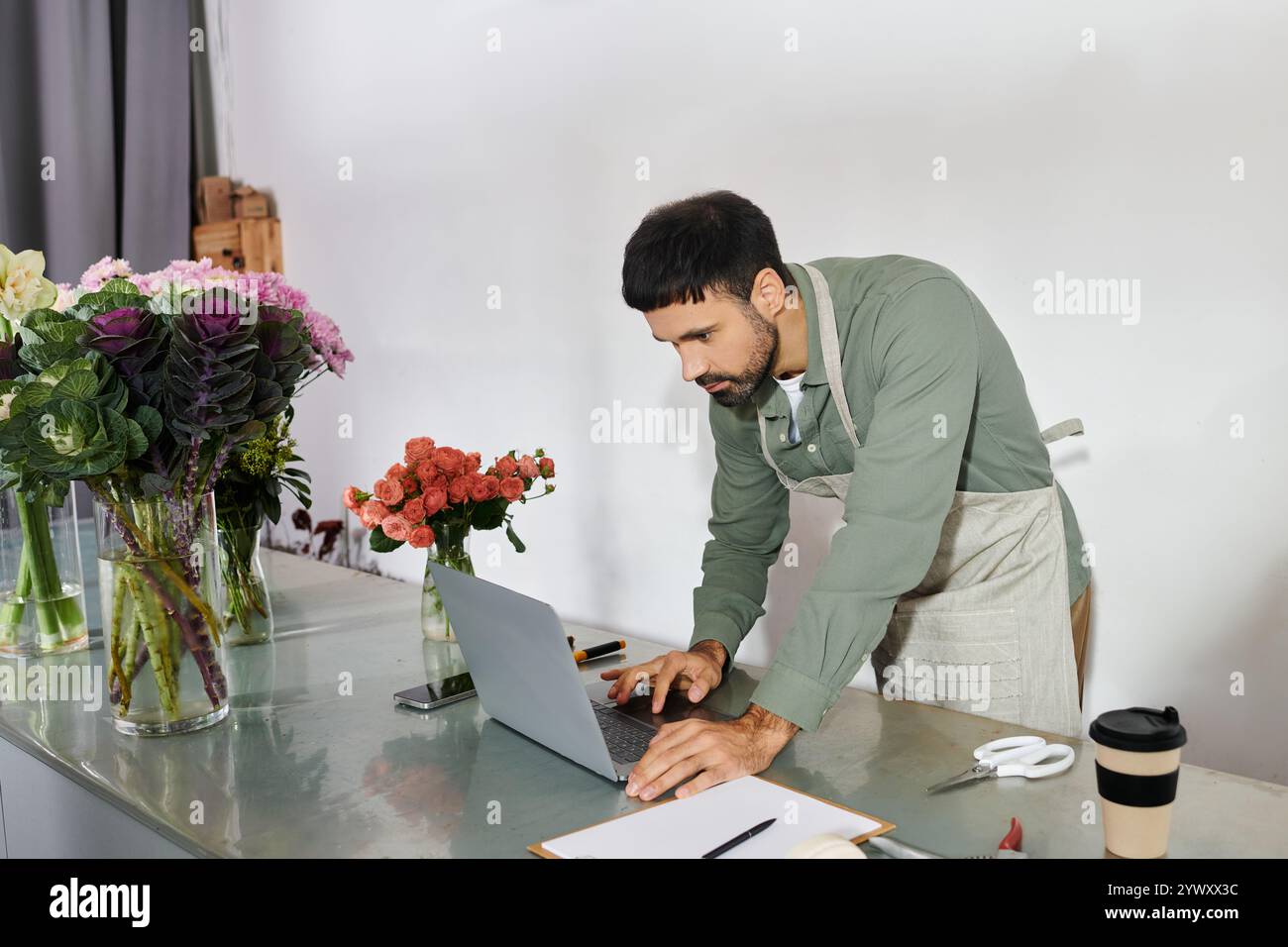 Un fiorista esperto si concentra sul suo notebook in mezzo a una varietà di fiori colorati e vegetazione. Foto Stock