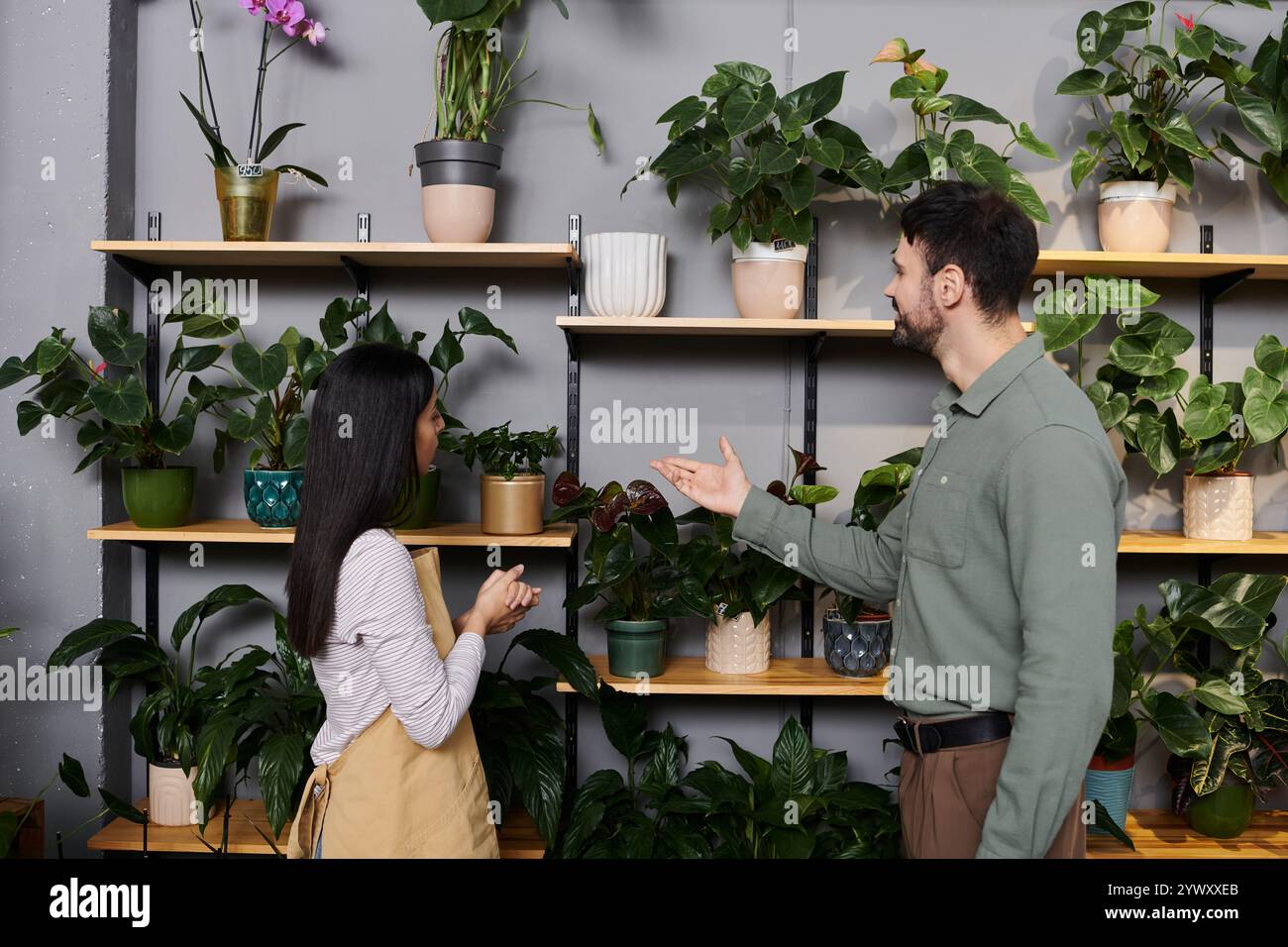 Un bellissimo fiorista si impegna con un cliente mentre è circondato da piante e fiori vivaci. Foto Stock