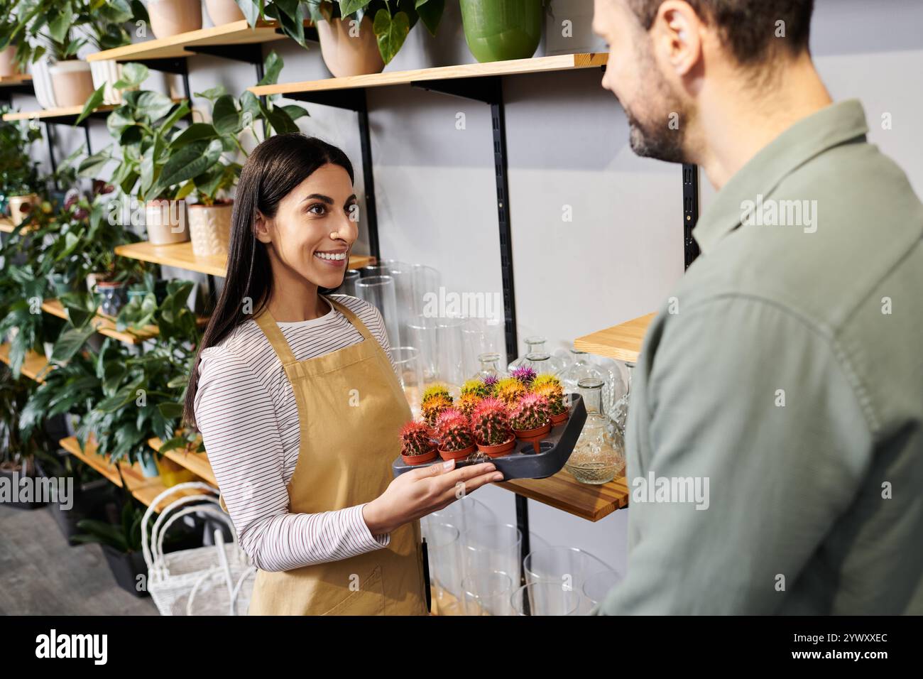Il bellissimo fioraio si impegna con un cliente maschile mentre espone piante colorate nel negozio. Foto Stock