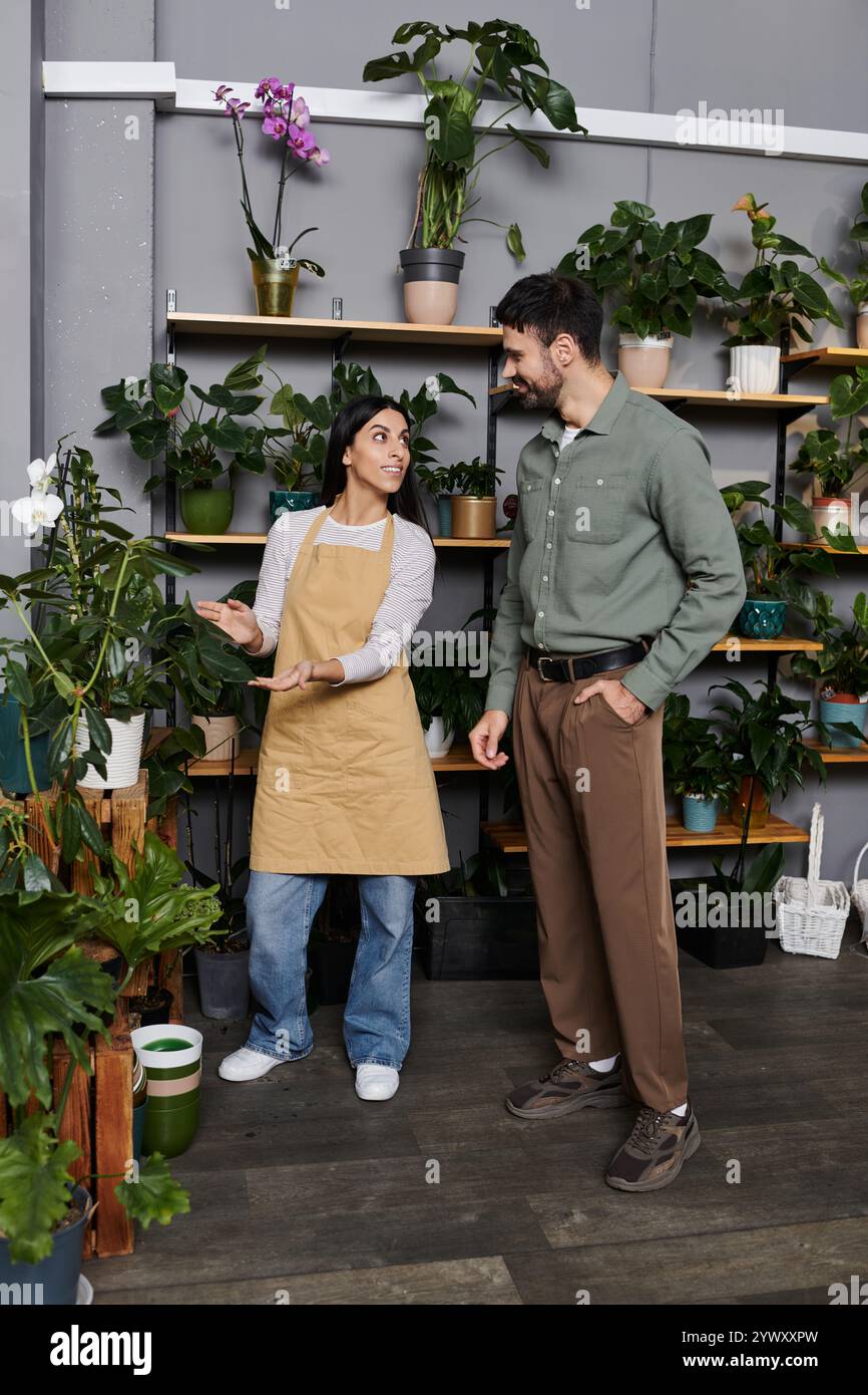 Florist aiuta un cliente maschile a esplorare piante vivaci in un affascinante ambiente di fioreria. Foto Stock