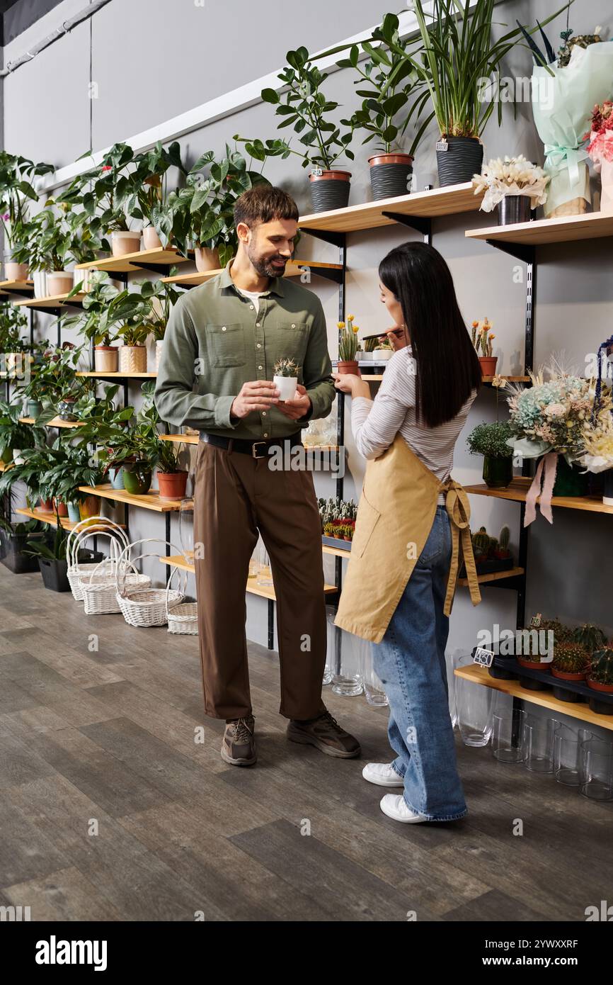 Florist si impegna con un cliente maschile, guidandolo attraverso una varietà di piante verdi lussureggianti. Foto Stock