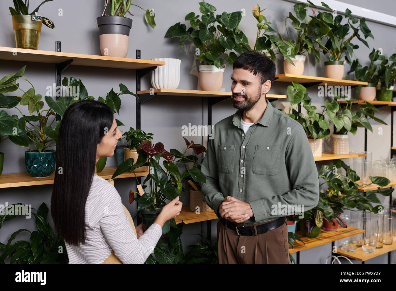 Un fioraio professionista si impegna con un cliente maschile in un negozio vivace ed ecologico. Foto Stock