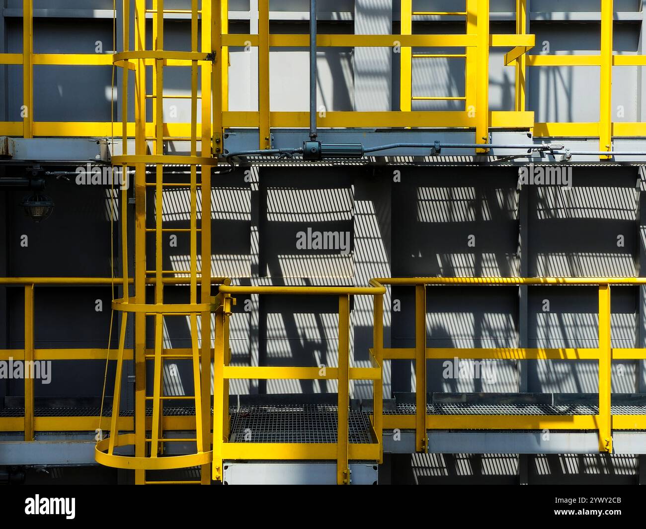 Una scala gialla è attaccata al lato di un edificio grigio. La scaletta è posizionata ad angolo, consentendo un facile accesso ai livelli superiori del Foto Stock