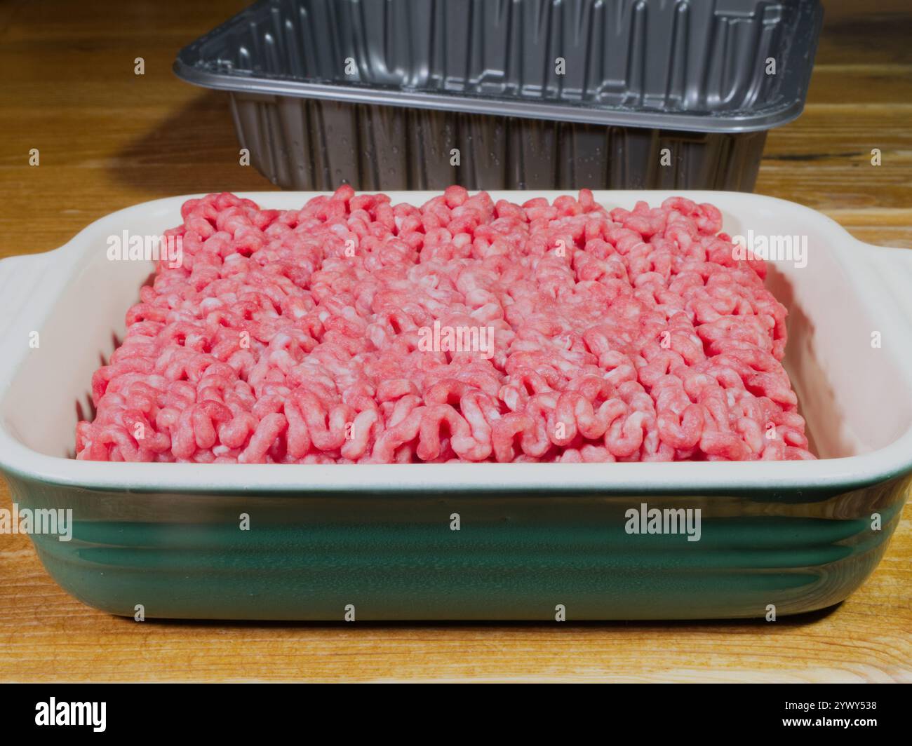 Primo piano di carne di manzo macinata fresca e cruda, appena prelevata da un vassoio di plastica e riposata in un piatto di ceramica prima di cucinare. Foto Stock