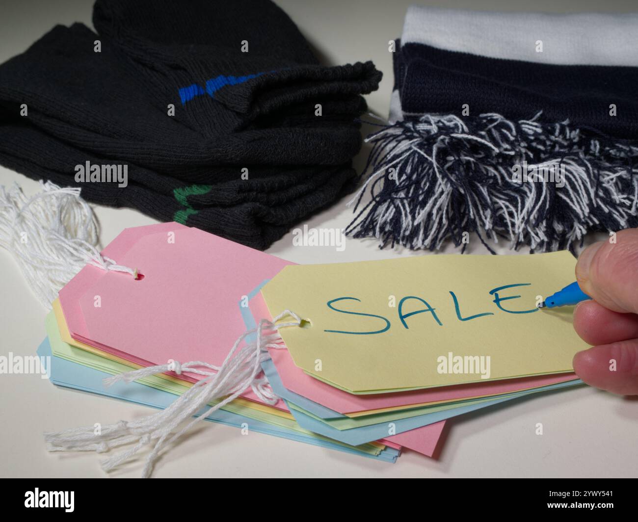 Primo piano di paia di calzini nuovi e una sciarpa, con cartellini o etichette colorate davanti, e una mano che utilizza un pennarello per scrivere LA VENDITA su uno di essi. Foto Stock