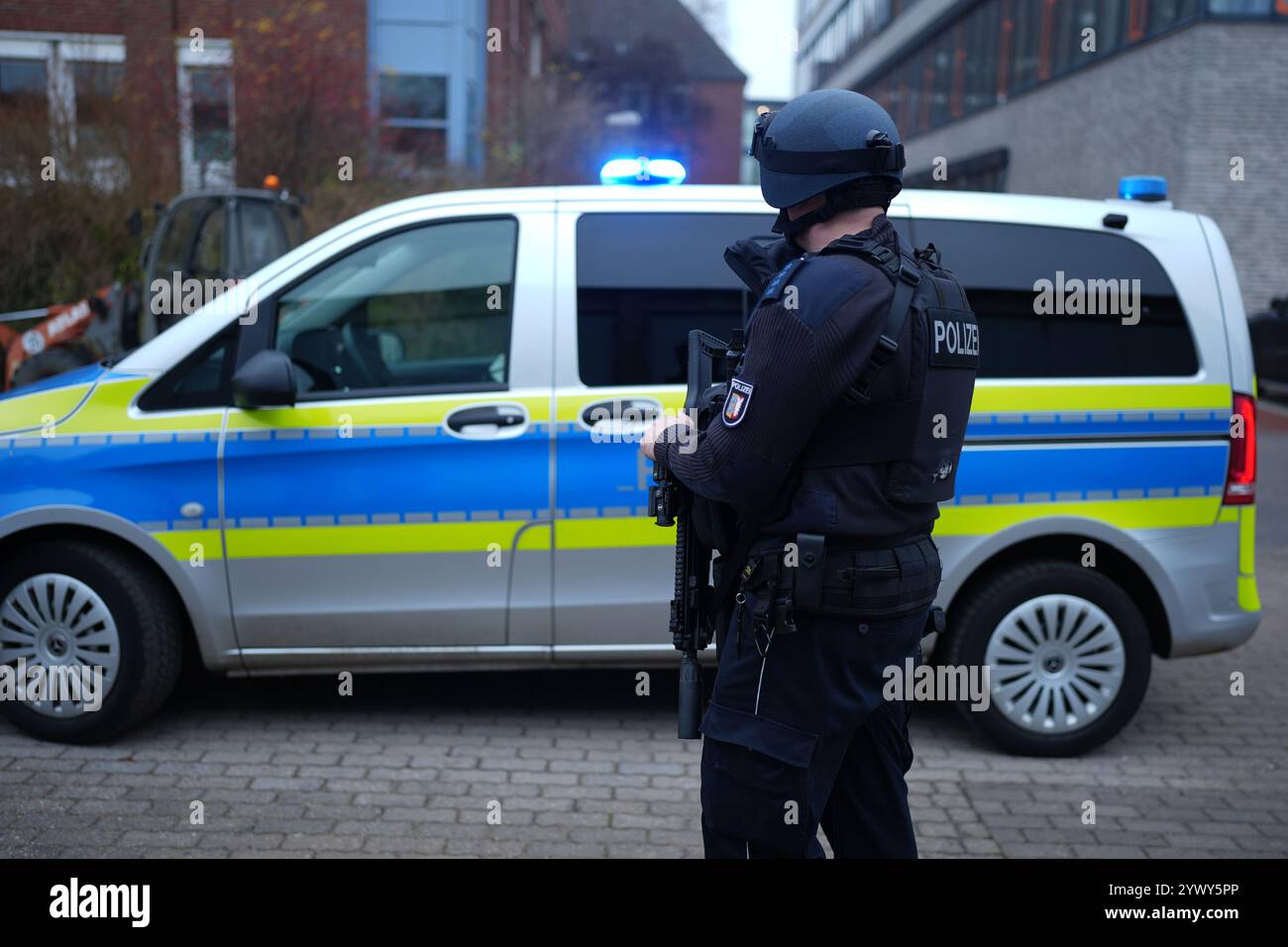 Kiel, Germania. 11 dicembre 2024. ILLUSTRAZIONE - Un agente di polizia indossa un casco balistico e tiene in mano un fucile HK 437 a medio raggio di fronte alla sua auto di pattuglia sul terreno del centro di polizia di Eichhof. Crediti: Marcus Brandt/dpa/Alamy Live News Foto Stock