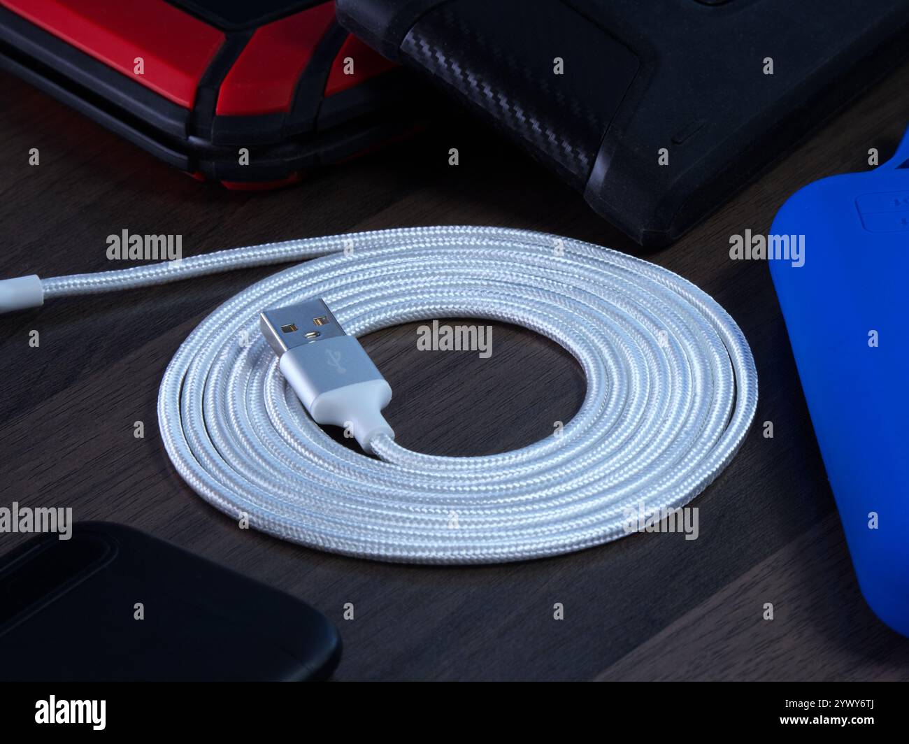 Primo piano di un cavo o cavo USB di tipo A bianco A spirale, utilizzato per trasferire o trasmettere dati o collegare l'alimentazione, circondato da dischi rigidi di backup esterni. Foto Stock