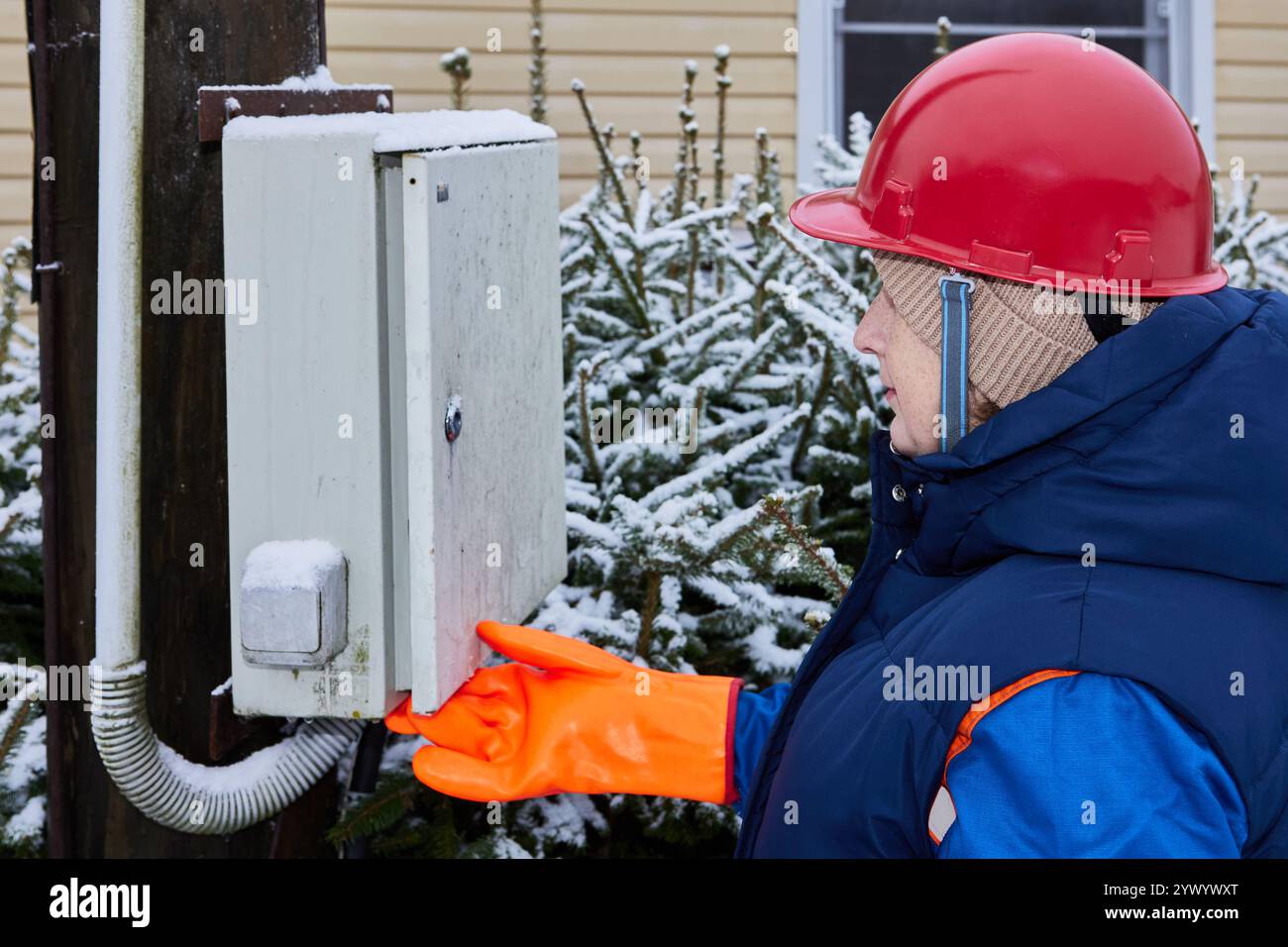 Utilizzo di guanti dielettrici per aprire una scatola elettrica all'aperto mentre l'elettricista della società elettrica ispeziona le apparecchiature elettriche di consumo nella comunità. Foto Stock