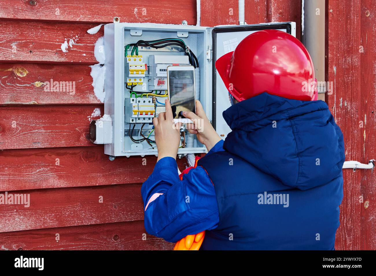 Un dipendente di un'azienda di vendita di energia rileva le letture dei contatori elettrici esterni in casa in inverno utilizzando una fotocamera per smartphone. Foto Stock