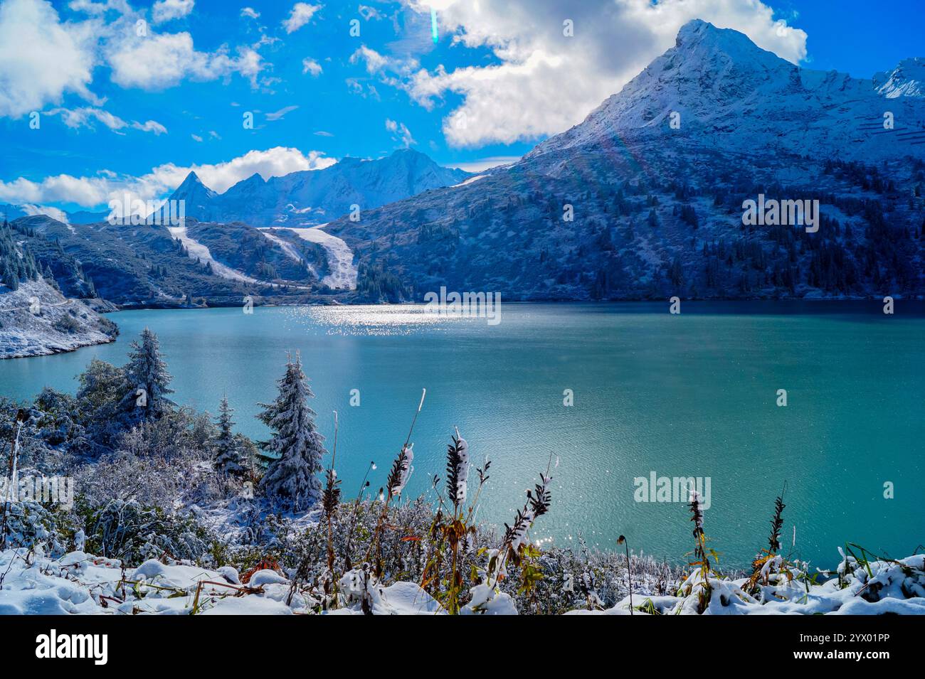 Una vista del pittoresco lago alpino, il Kops Reservoir, con acqua verde e riflessi, circondato da montagne innevate. In primo piano - S. Foto Stock