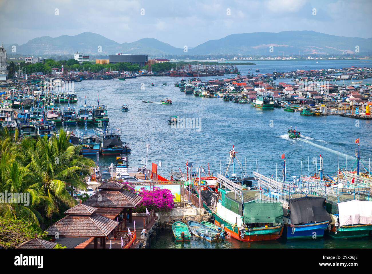 Vista panoramica di un vivace porto con barche da pesca e vegetazione lussureggiante Foto Stock