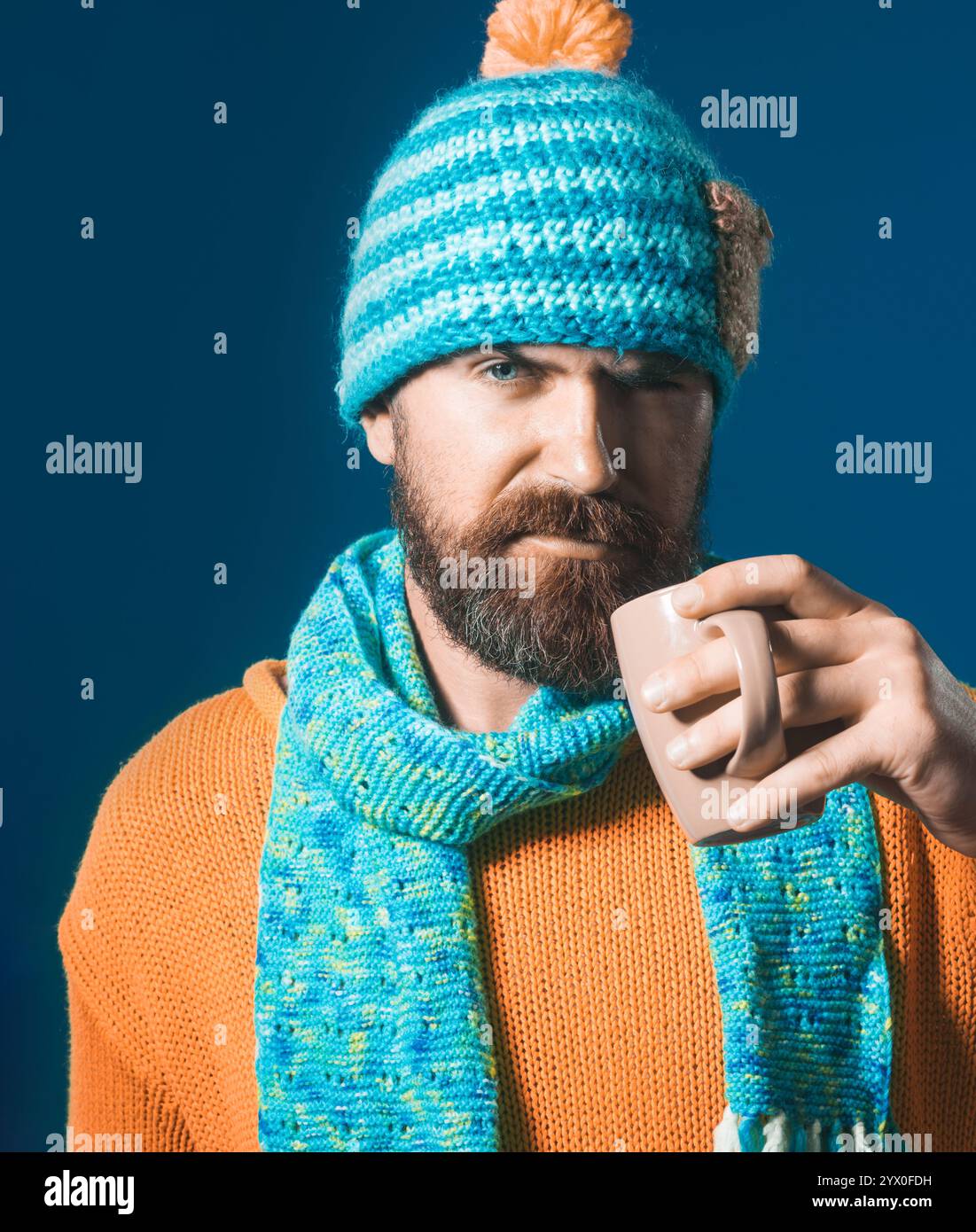 L'ora del caffè. Ritratto ravvicinato di un uomo barbuto serio con maglione a maglia, cappello e sciarpa bevendo una tazza di tè o caffè. Bell'uomo con barba e mus Foto Stock