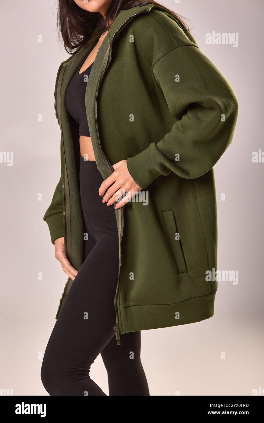 Ritratto di una donna vestita con cappuccio verde e leggings neri, stile casual, con un concetto di moda neutro Foto Stock