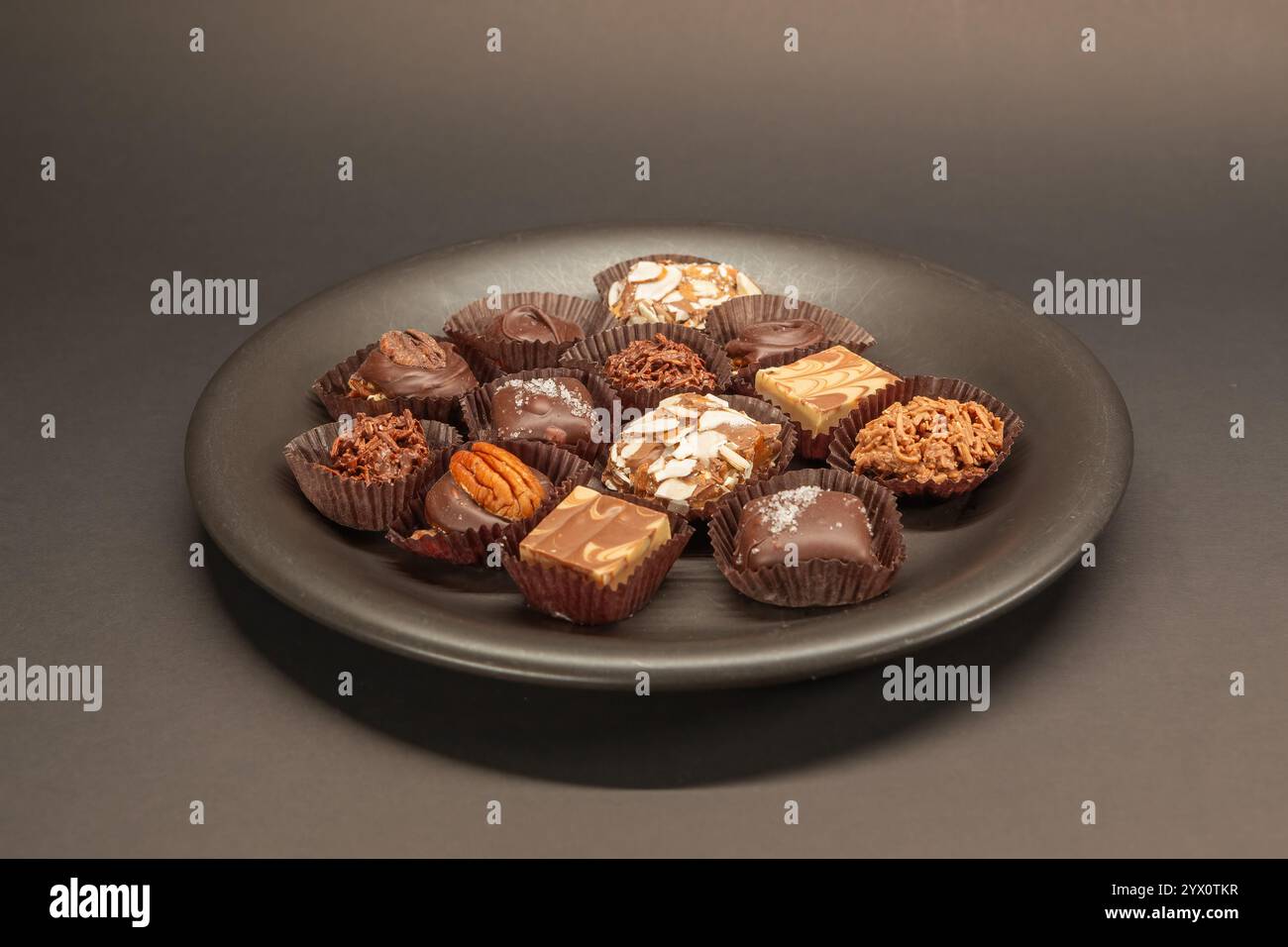 Cioccolatini artigianali realizzati a mano disposti splendidamente su un piatto marrone scuro su un ricco sfondo scuro. Foto Stock