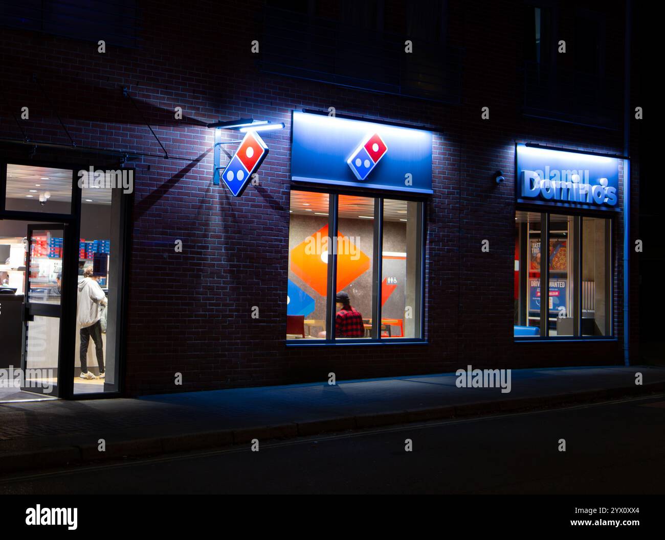 Esterno illuminato di sera di un ristorante pizzeria Domino's con cartellonistica visibile e clienti all'interno di Calne Wiltshire UK Foto Stock
