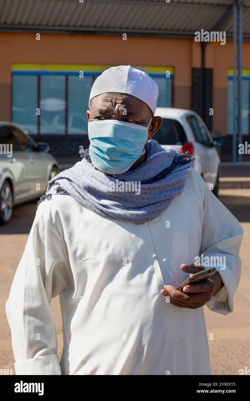 Ritratto di un vecchio musulmano africano che parla sullo smartphone che cammina per strada, con cappello di preghiera taqiyah kufi, uomini Islam all'aperto Foto Stock