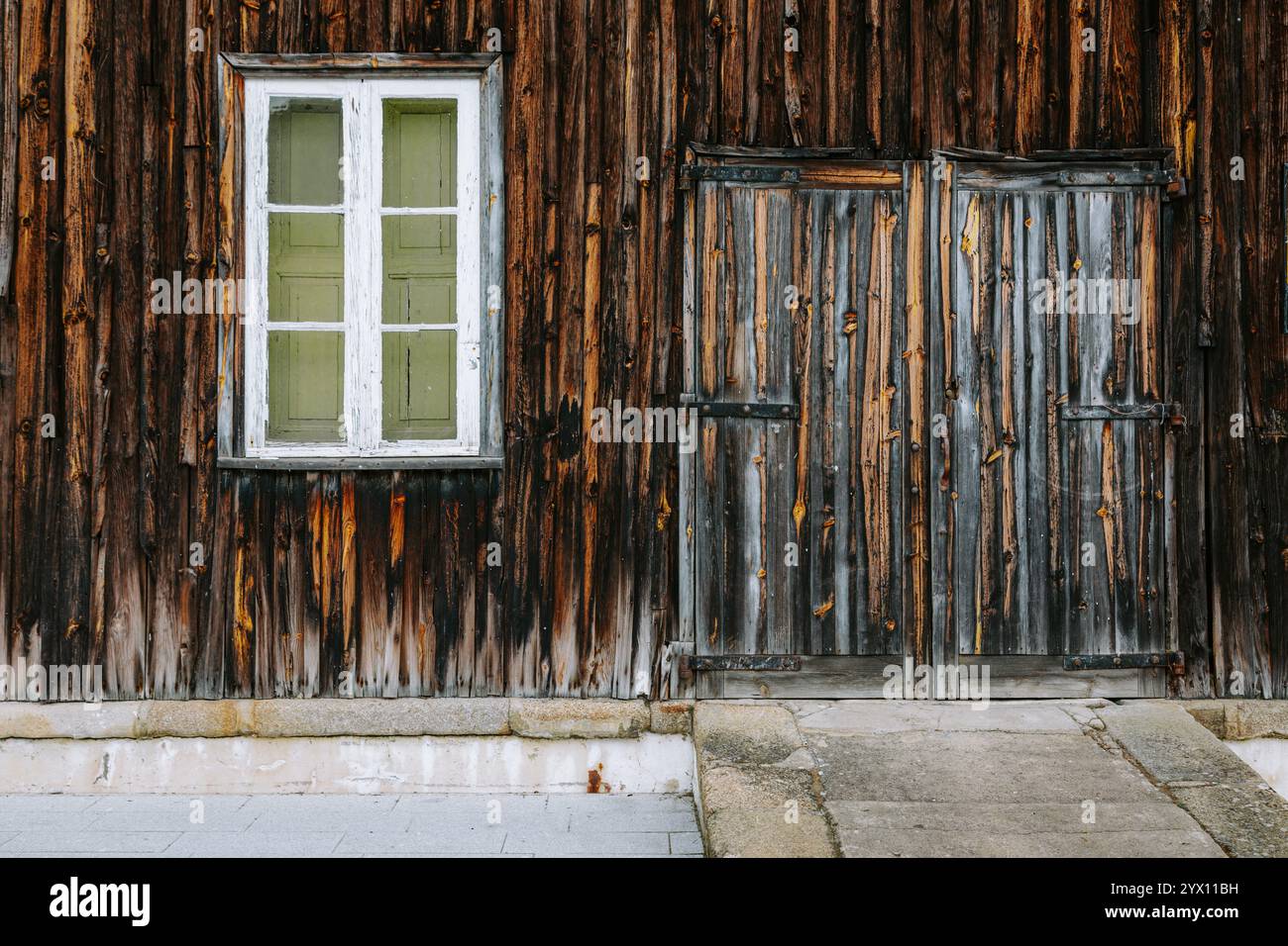 La facciata in legno di un edificio ad alijo, portogallo, presenta una doppia porta chiusa e una finestra, che mostra gli effetti del tempo e del tempo Foto Stock