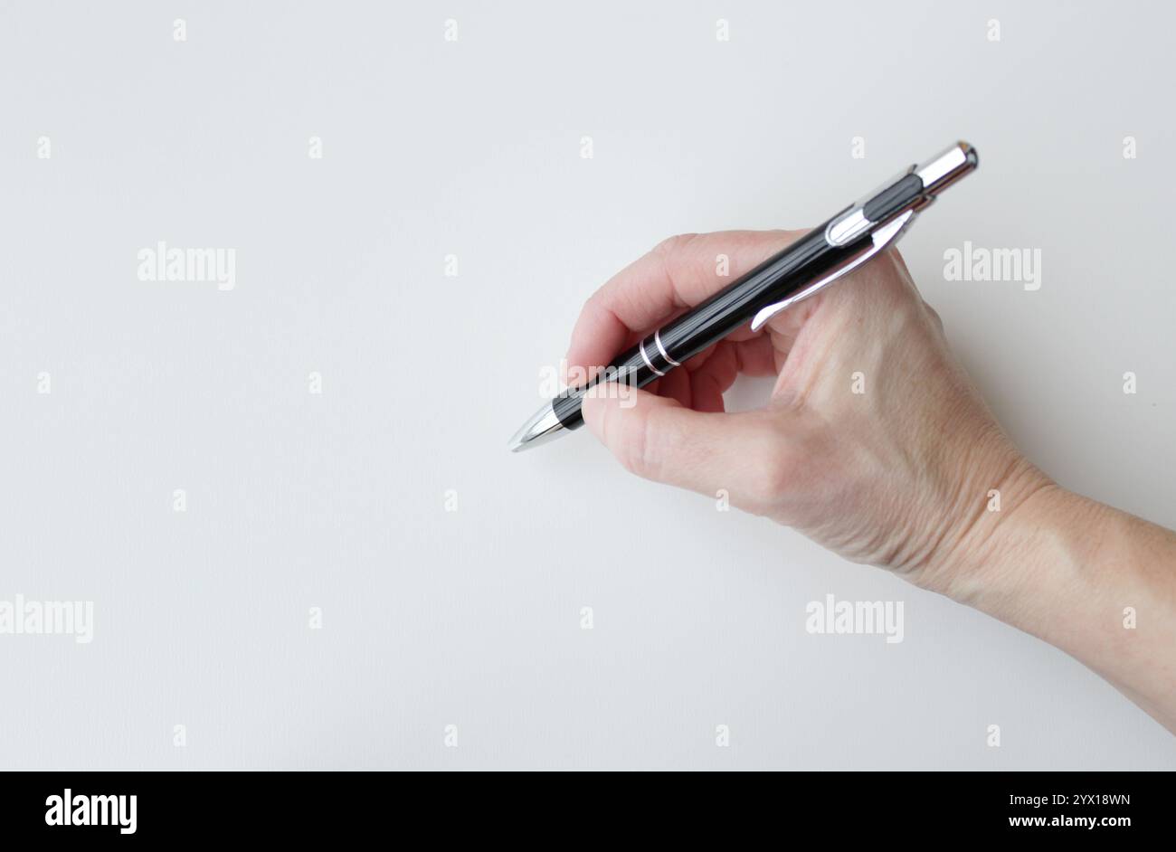 Mano caucasica con una penna nera per scrivere un messaggio o firmare un documento. Scrittura, forniture per l'ufficio. Spazio di copia disponibile su sfondo bianco. Foto Stock