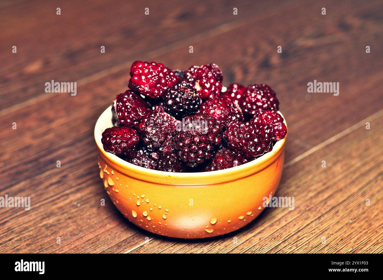 Blackberries fresche in una vivace ciotola arancione su una superficie di legno Foto Stock