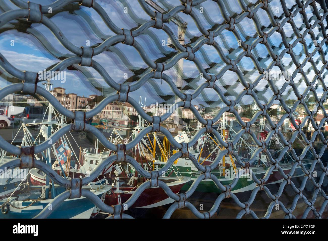 Una vetrina con vetrina con copertura e modelli di barche da pesca riflette il lungomare del villaggio di Saint-Jean-de-Luz, Francia. Il villaggio cade lungo t Foto Stock