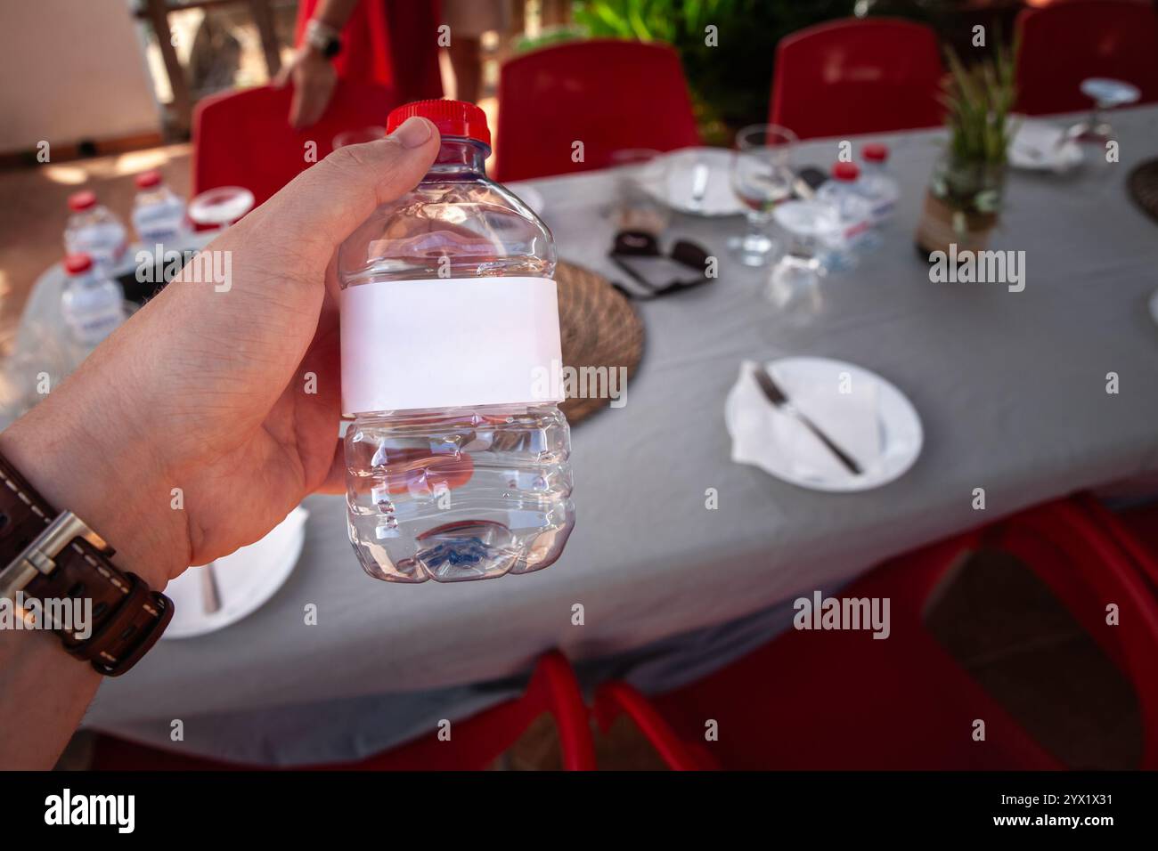 Una mano regge una piccola bottiglia di acqua sorgiva con un'etichetta bianca vuota. Il design semplice e trasparente attende il branding personalizzato, che simboleggia l'idr quotidiano Foto Stock