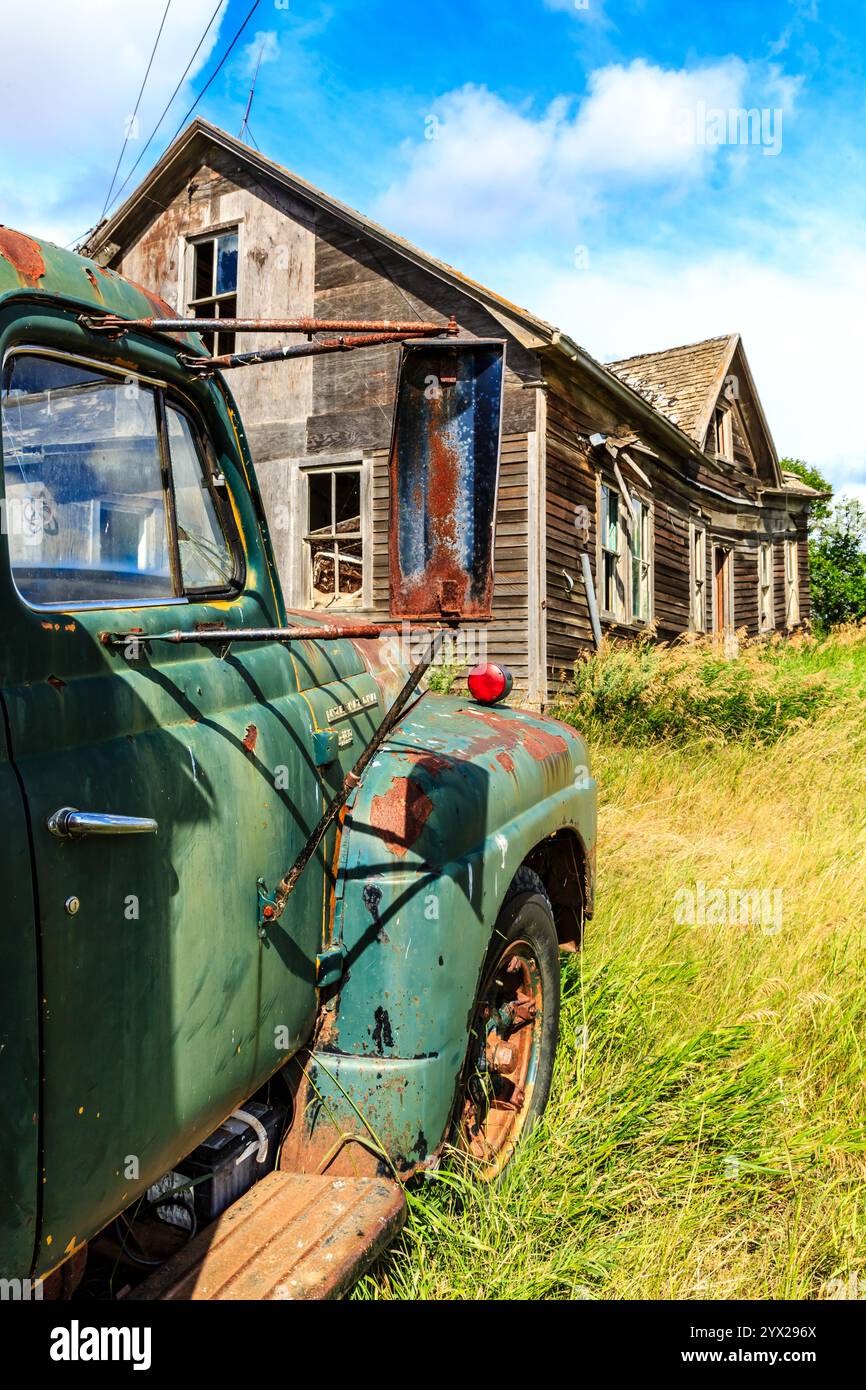Un vecchio camion verde è parcheggiato davanti a una casa. La casa è vecchia e malandata, con molta ruggine. Il carrello è parcheggiato davanti alla casa, Foto Stock
