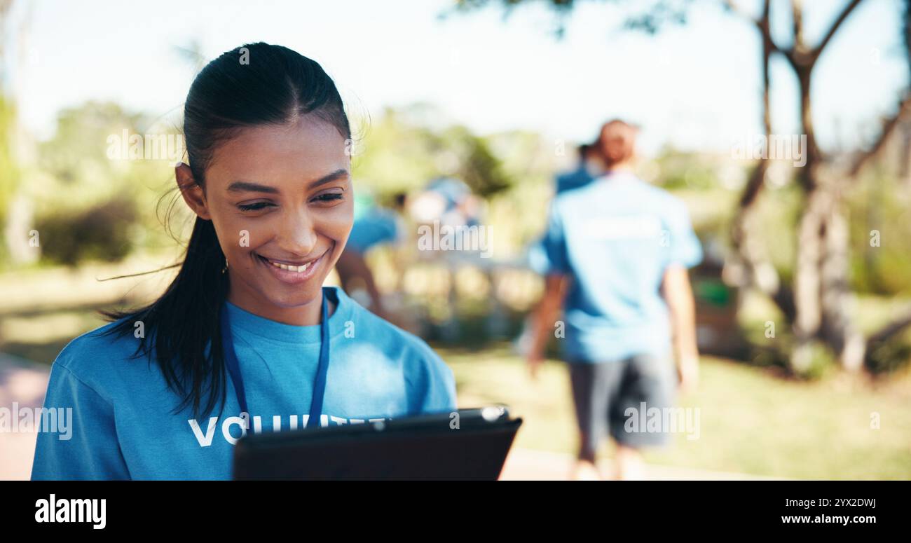 Beneficenza, sorriso e tablet con donna volontaria all'aperto nel parco per un'iniziativa alimentare comunitaria o una donazione. Attivismo, lista di controllo e programma con Happy Foto Stock