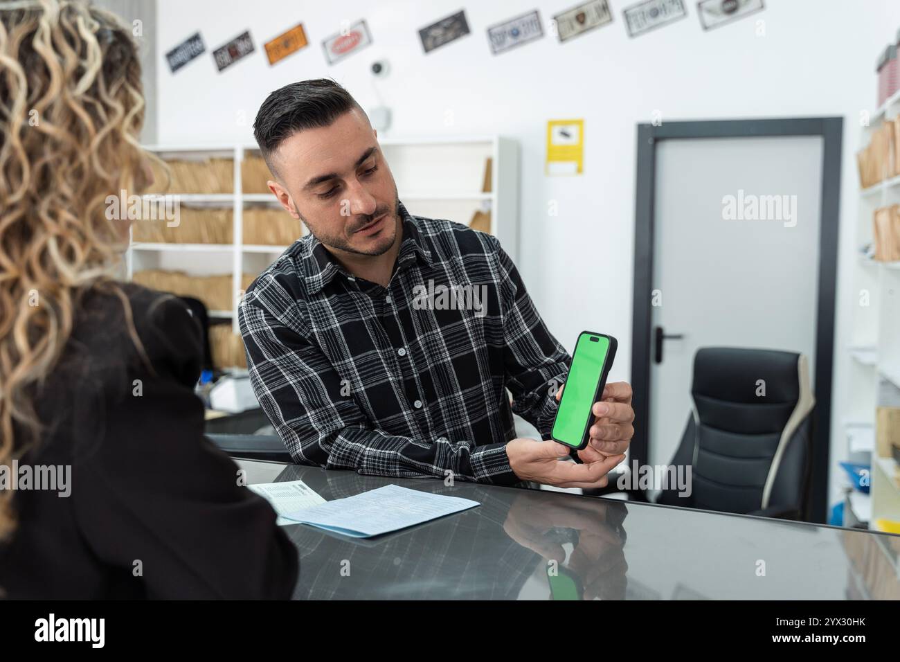 Uomo d'affari che mostra uno smartphone con schermo verde a un cliente durante una consulenza finanziaria in un ufficio Foto Stock