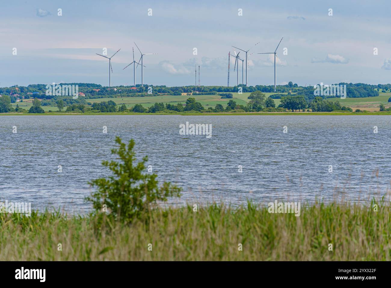 Una vista dei mulini a vento che generano energia elettrica da fonti rinnovabili su una piccola collina dietro un incantevole lago. Foto Stock