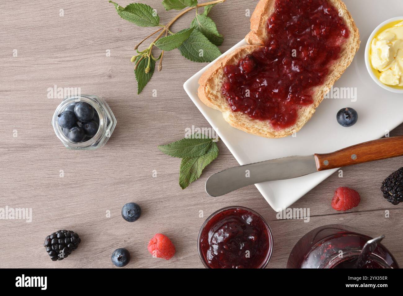 Brinda con marmellata di frutta di bosco su un piatto bianco su una panchina di legno con vasetti e frutti di bosco. Vista dall'alto. Foto Stock