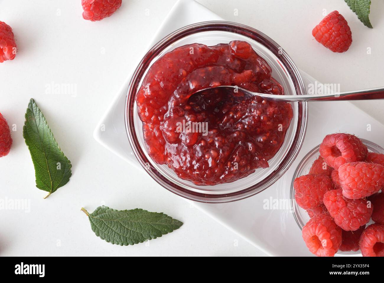 Dettaglio del piatto con ciotole di marmellata di lamponi e frutti di bosco sul tavolo bianco. Vista dall'alto. Foto Stock