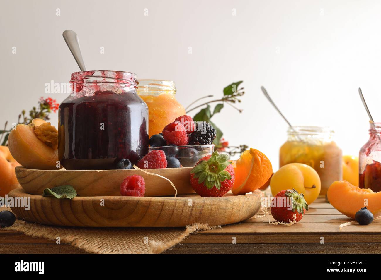 Diversi vasetti di marmellata di vari sapori con frutta diversa su un rustico tavolo in legno e sfondo bianco isolato. Vista frontale. Foto Stock