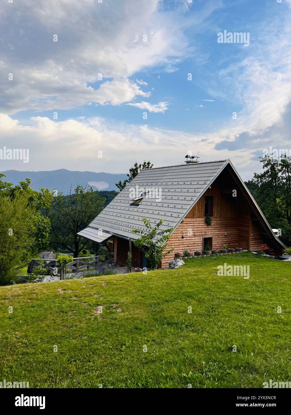 Una pittoresca cabina in legno circondata dal verde con una splendida vista sulle montagne sotto un cielo parzialmente nuvoloso. Ambiente perfetto per un tranquillo rifugio Foto Stock