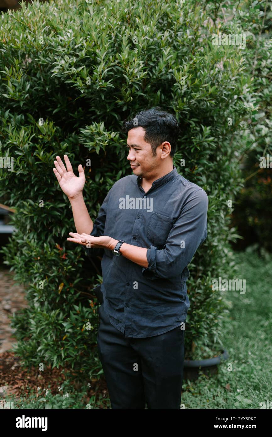Un uomo del sud-est asiatico che punta a qualcosa nella sua mano, evidenziando l'oggetto con interesse. Perfetto per dimostrazioni di prodotti, stile di vita o inst Foto Stock