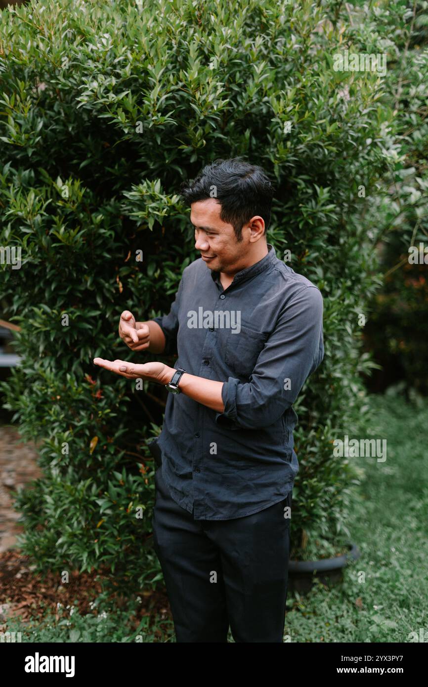 Un uomo del sud-est asiatico che punta a qualcosa nella sua mano, evidenziando l'oggetto con interesse. Perfetto per dimostrazioni di prodotti, stile di vita o inst Foto Stock