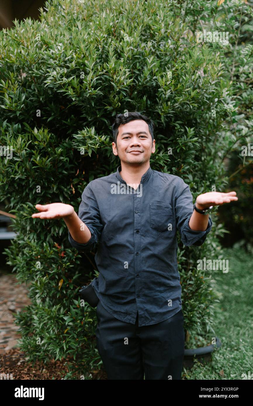 Un uomo del sud-est asiatico che fa una domanda con le mani aperte, mostrando curiosità e coinvolgimento. Perfetto per la comunicazione, lo stile di vita o concettuale Foto Stock