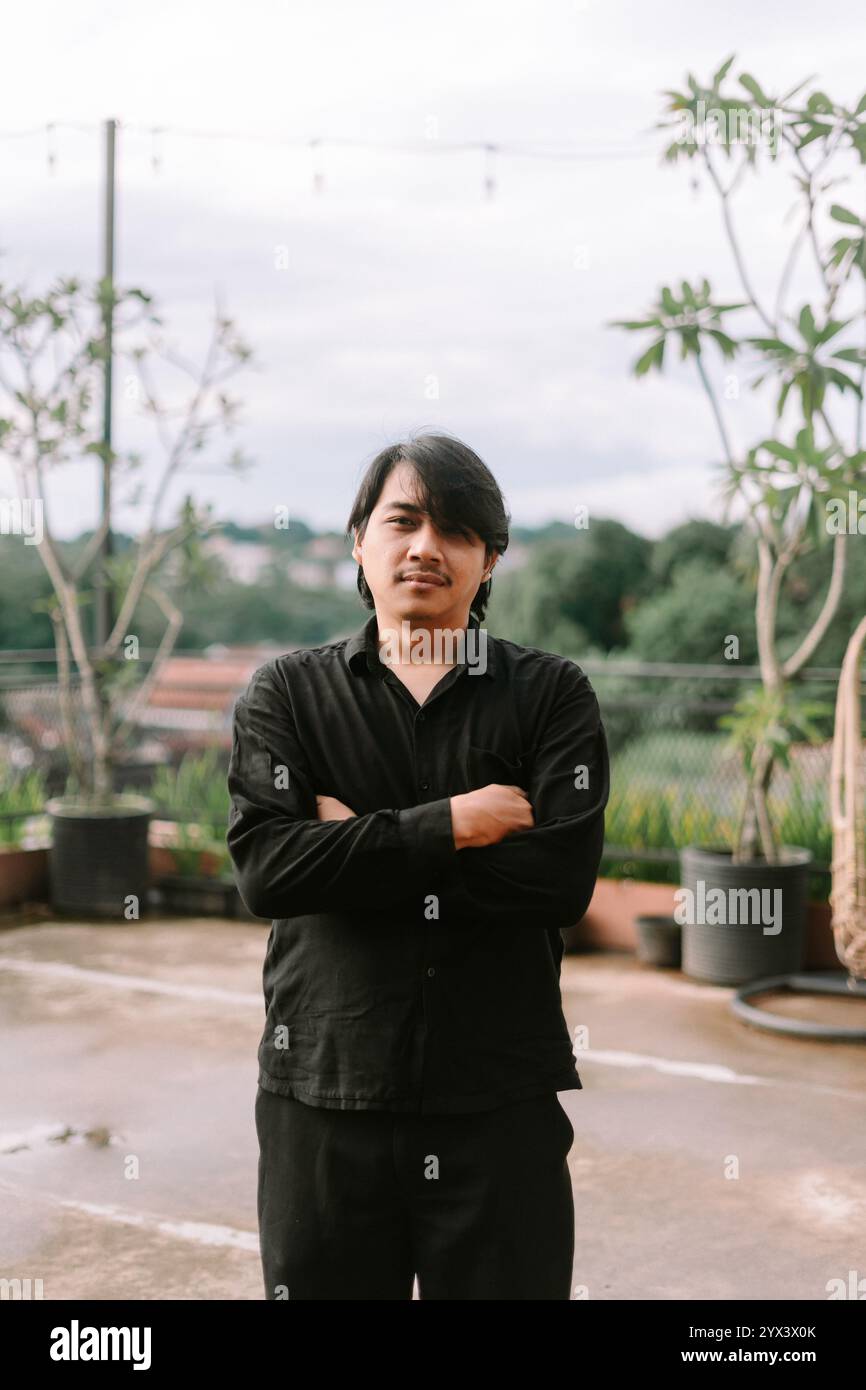 Un uomo del sud-est asiatico che attraversa le braccia, trasudando fiducia e contemplazione. Perfetto per progetti di stile di vita, ritratti o concettuali che presentano atti Foto Stock
