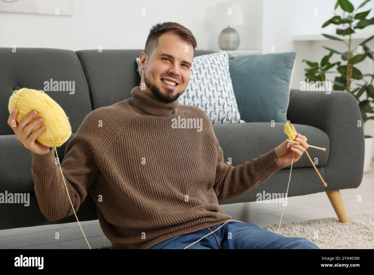 Uomo con filato giallo e aghi per maglieria a casa Foto Stock