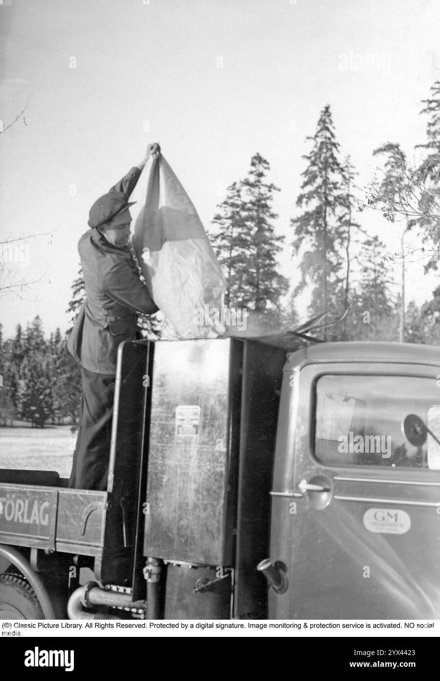 Gas di legno 1942. Un uomo riempie più carbone nel contenitore per alimentare l'unità gas di legno. Una caratteristica naturale durante questi anni durante la seconda guerra mondiale era l'unità di gassificazione Wood su auto e camion. Il gas di legno è un gas che deriva dalla combustione incompleta di legno o carbone ed è stato utilizzato per alimentare i veicoli. Il conducente doveva riempire il carbone da solo e assicurarsi che la combustione funzionasse come dovrebbe. A causa della mancanza di carburante durante la seconda guerra mondiale, il gas di legno giocò un ruolo importante nel mantenere i trasporti in funzione. Foto Stock