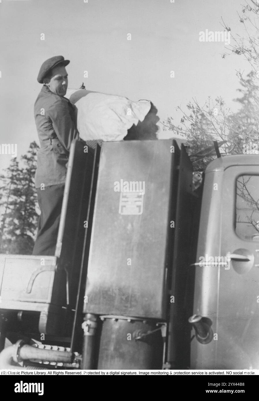 Gas di legno 1942. Un uomo riempie più carbone nel contenitore per alimentare l'unità gas di legno. Una caratteristica naturale durante questi anni durante la seconda guerra mondiale era l'unità di gassificazione Wood su auto e camion. Il gas di legno è un gas che deriva dalla combustione incompleta di legno o carbone ed è stato utilizzato per alimentare i veicoli. Il conducente doveva riempire il carbone da solo e assicurarsi che la combustione funzionasse come dovrebbe. A causa della mancanza di carburante durante la seconda guerra mondiale, il gas di legno giocò un ruolo importante nel mantenere i trasporti in funzione. Foto Stock