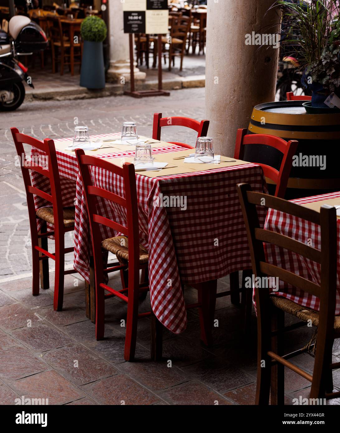 Tavoli e sedie vuoti all'esterno di un ristorante sotto gli iconici portici della città, con tavoli che presentano il classico tavolo italiano a scacchi rosso e bianco Foto Stock